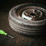 Un pneu de voiture et un tournevis vert placés sur le sol du garage, représentant la réparation automobile.